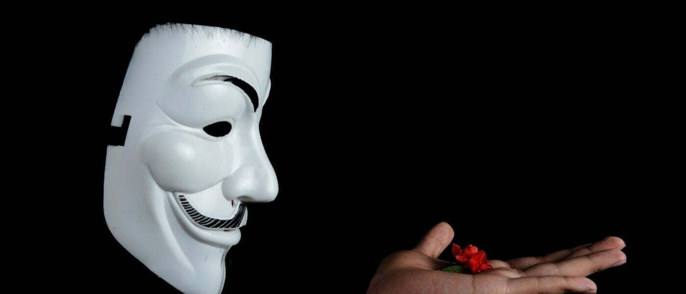 photo of guy fawkes mask with red flower on top on hand